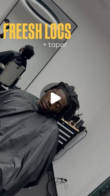 Client with freshly retwisted locs and a clean taper, reclined in the barber chair